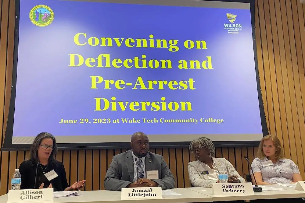 four people at a table giving in presentation. Behind them is a screen that says "Convening on Deflection and Pre-Arrest Diversion"