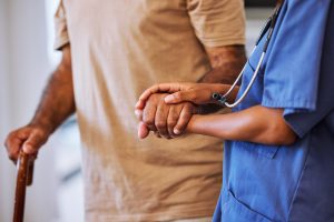 A medical professional holds the hand of an elderly person using a cane