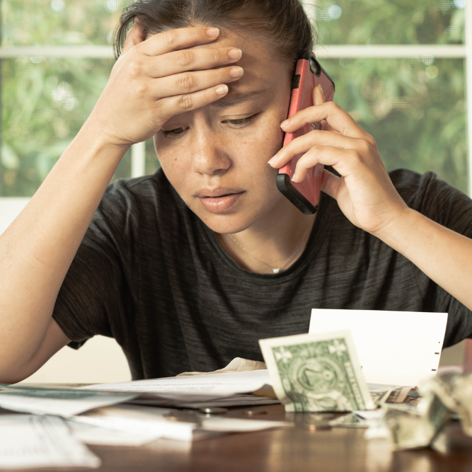 Bills Person on the phone looking worried with bills on the table in front of them