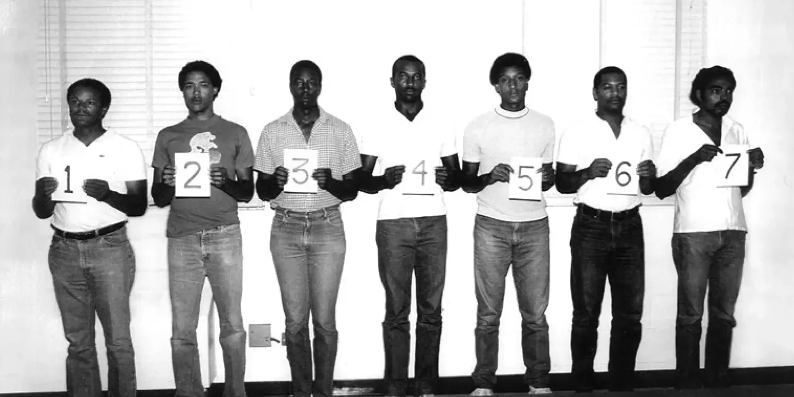 7 men standing side by side holding numbers 1-7